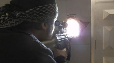 A member of the Free Syrian Army points his weapon through a hole in a wall as he takes up a defense position in Daraya