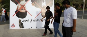 Pro-government protesters walk past a defaced banner showing Iran's Supreme leader Ayatolla Khomani and President Ahmedanijad's at a rally to show support towards GCC Union, in al Fateh Grand Mosque in Manama