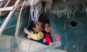 Esma, 7, and a friend peer out of a tent in Lebanon that has been home to her family since last year