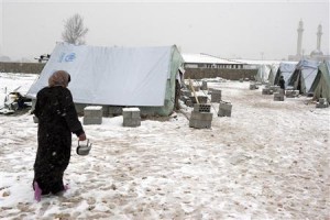 A Syrian refugee woman holds a pot as she walks in snow outside their tents during a winter storm in al-Marj, in the Bekaa valley