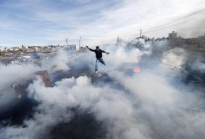 A Palestinian protester jumps as tear gas fired by Israeli soldiers rises during clashes in Jalazoun refugee camp near Ramallah