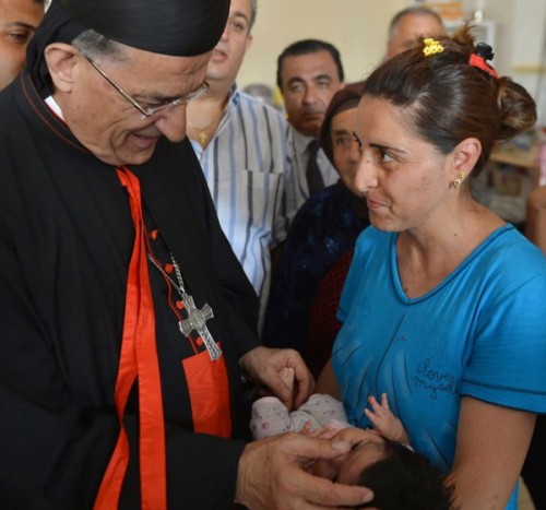 Lebanese Cardinal Bechara Rai, the patriarch of Maronite Catholics who headed a delegation of Catholic and Orthodox patriarchs to Iraq Aug. 20, blesses a baby in Irbil. (CNS/Courtesy Maronite Patriarchate)