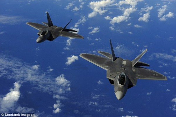 A pair of U.S.-built NORAD F-22 fighter jets fly  over a mountainous area of Alaska,