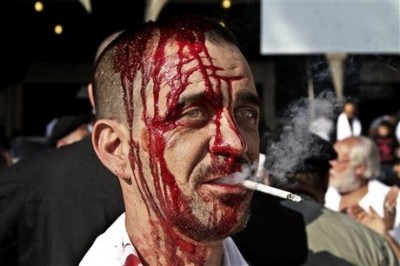 A Lebanese Shiite smokes a cigarette as he bleeds from his head from self inflicted wounds, during Ashoura in the southern market town of Nabatiyeh, Lebanon, Thursday, Nov. 14, 2013. Thursday's commemorations marked the climax of Ashoura, the yearly mourning period in which Shiite Muslims remember the seventh century death of the Prophet Muhammad's grandson, Imam Hussein, in a battle in the central city of Karbala. (AP Photo/Mohammed Zaatari)