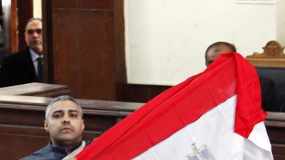 Al Jazeera journalist Mohamed Fahmy raises an Egyptian national flag while talking to the judge during his retrial at a court in Cairo February 12, 2015. The two remaining Al Jazeera journalists, Mohamed Fahmy and Baher Mohamed, were released from an Egyptian jail on Thursday after more than 400 days, but the court said the case against them was still pending.