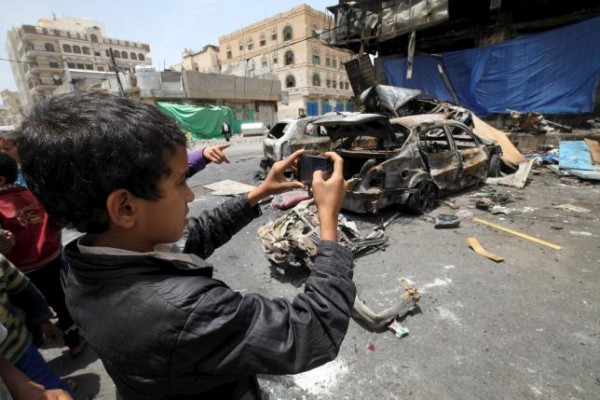 A boy takes pictures for the wreckage of a car at the site of a car bomb attack in Yemen's capital Sanaa June 18, 2015. REUTERS/Mohamed al-Sayaghi