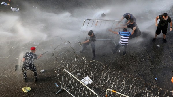 Lebanese activists, right, remove barriers as they try to cross to the government house, as riot police spray them with water cannons during a protest  on Aug 22, 2015