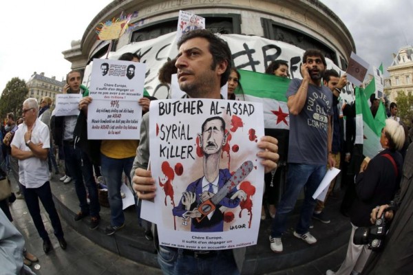 A protester holds a placard with a painting of Bashar al-Assad reading 'Butcher Al Assad, Syrial Killer - Dear Europe, It only needs to get one out, not to have to welcome millions.'