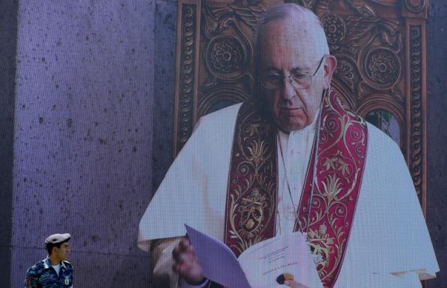 A police officer stands in front of a screen showing Pope Francis during the Divine Liturgy at the apostolic Cathedral in Etchmiadzin, Armenia, June 26, 2016. REUTERS/David Mdzinarishvili