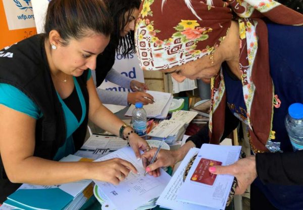 A Syrian refugee woman, right, signs documents after she received a new debit bank card through which all aid agencies transfer their aid at a distribution center, in Bar Elias town, in Lebanon's Bekaa valley, Tuesday, Oct. 25, 2016. Distribution of this 'joint card' began earlier this month. It replaces separate cards for food, cash and other aid. 