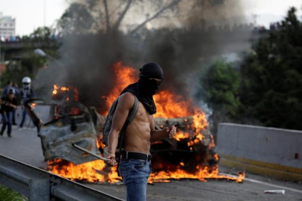 A demonstrator stands near fire during a rally against Venezuela's President Nicolas Maduro in Caracas. REUTERS/Carlos Garcia Rawlins