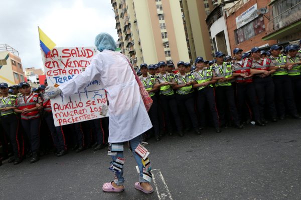 A woman holds a placard in front of riot police during a rally of health-sector workers and opposition supporters, due to the shortages of basic medical supplies and against Venezuelan President Nicolas Maduro's government in Caracas, Venezuela, February 7, 2017. The placard reads, "Help us, the patients are dying."REUTERS/Carlos Garcia Rawlins 