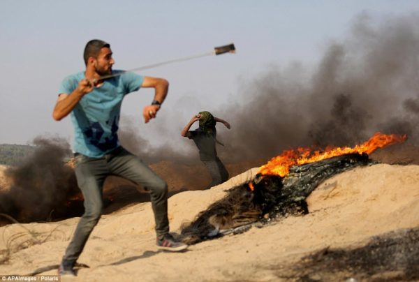 A Palestinian protester hurls stones towards Israeli security forces during clashes near the border between Israel and central Gaza Strip 
