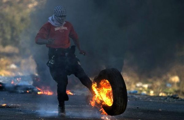 A Palestinian kicks a burning tire during clashes with Israeli troops at a protest against U.S. President Donald Trump's decision to recognize Jerusalem as Israel's capital, near the Jewish settlement of Beit El, near the West Bank city of Ramallah December 10, 2017. REUTERS/Mohamad Torokman