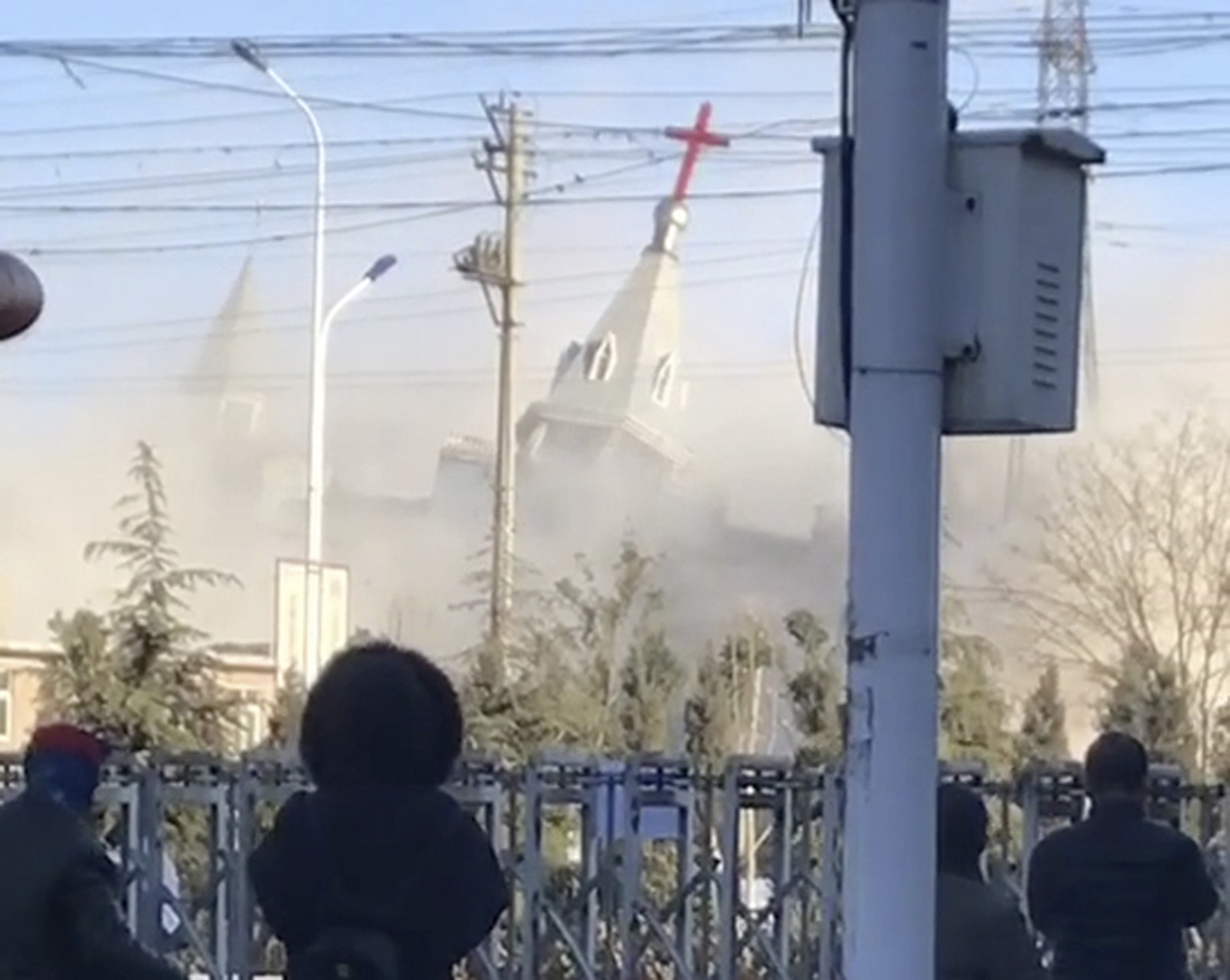 In this image taken from video shot Tuesday, Jan. 9, 2018, by China Aid and provided to the Associated Press, people watch the demolition of the Golden Lampstand Church in Linfen in northern China's Shanxi province. Witnesses and overseas activists say paramilitary troops known as the People's Armed Police used excavators and dynamite on Tuesday to destroy the Golden Lampstand Church, a Christian mega-church that clashed with the government. (China Aid via AP)