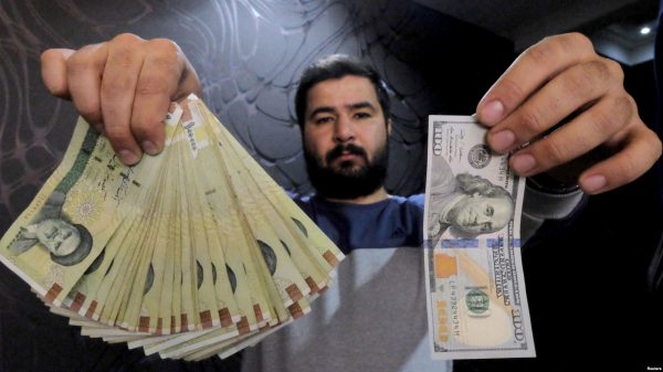 A money changer poses for the camera with a U.S dollar (R) and the amount being given when converting it into Iranian rials (L), at a currency exchange shop at Tehran's business district. File photo