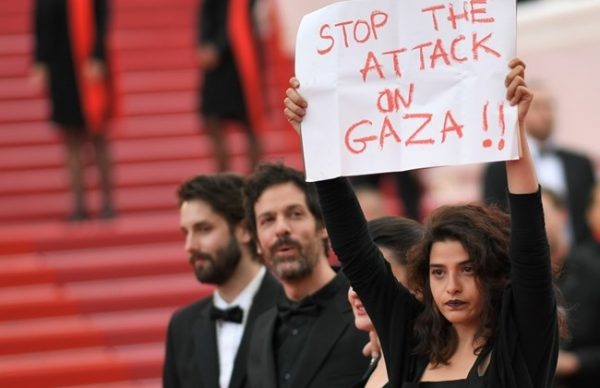 French-Lebanese actress Manal Issa (R) holds a sign reading "Stop the Attack on Gaza" as she arrives on May 15, 2018 with Syrian director Gaya Jiji (2ndR) and Greek-South African film director Etienne Kallos (2ndL) for the screening of the film "Solo : A Star Wars Story" at the 71st edition of the Cannes Film Festival in Cannes, southern France. / AFP / LOIC VENANCE