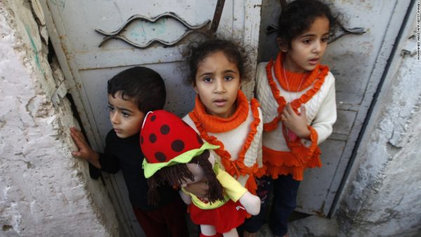 Palestinian children stand at the gate of their home as they watch a funeral procession
