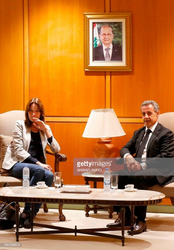 French-Italian musician Carla Bruni (L) and her husband, former French President Nicolas Sarkozy sit under a portrait of Lebanese president Michel Aoun as they arrive at the Beirut airport on July 29, 2018. - Bruni is set to perform her fifth album, French Touch, at the Beiteddine Art Festival on July 30. (Photo by ANWAR AMRO / AFP)        (Photo credit should read ANWAR AMRO/AFP/Getty Images)