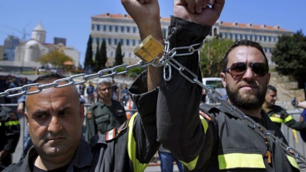 FILE - Civil Defense volunteers with symbolic metal chains around their wrists protest in front of the government building during a sit-in to demand full time jobs in fixed posts in Beirut, Lebanon, April 4, 2019.