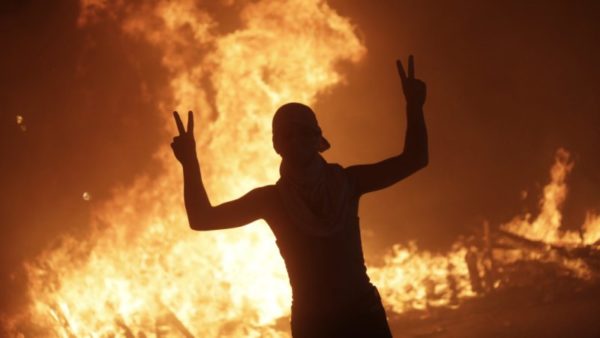 An anti-government protester makes victory signs in front a fire set by protesters to block a road during a demonstration in Beirut, Lebanon.CREDIT:AP