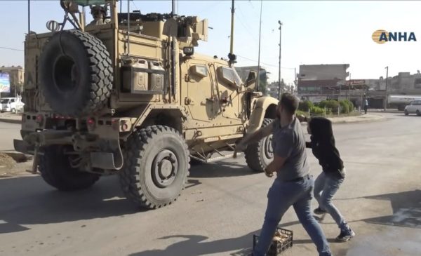 In this frame grab from video provided by Hawar News, ANHA, the Kurdish news agency, residents who are angry over the U.S. withdrawal from Syria hurl potatoes at American military vehicles in the town of Qamishli, northern Syria, Monday, Oct. 21, 2019. Defense Secretary Mark Esper said Monday in Afghanistan that U.S. troops will stay in eastern Turkey to protect Kurdish-held oil fields for at least the coming weeks and that he was discussing options to keep them there. (ANHA via AP)