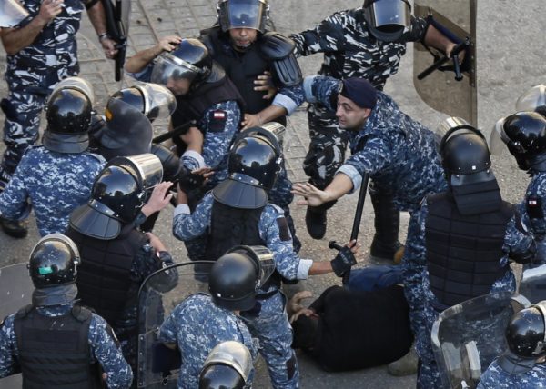 A riot police officer, center right, stops other policemen from beating a protester who lies on the ground, after clashes erupted between an anti-government protesters and Hezbollah supporters near the government palace, in Beirut, Lebanon, Tuesday, Oct. 29, 2019. Lebanon's prime minister resigned, bowing to one of the central demands of anti-government protests. (AP Photo/Hussein Malla)
